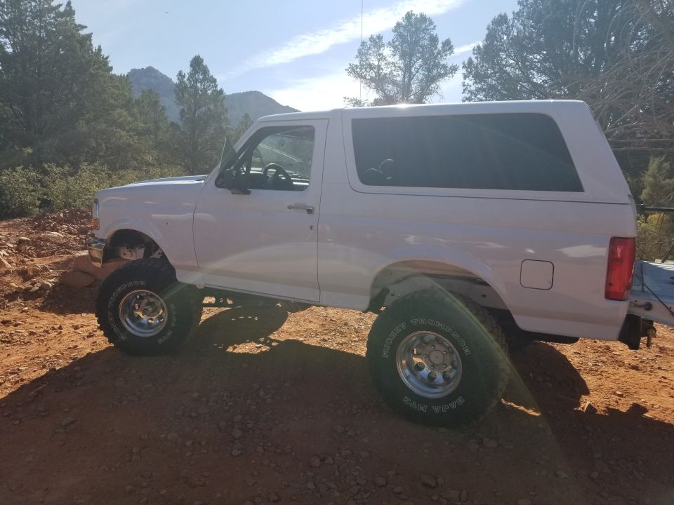 White 1995 Ford Bronco with off-road tires parked on a dirt road.