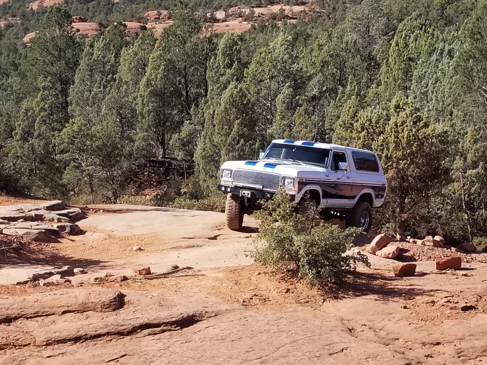 White and blue 1978-1979 Ford Bronco off-roading on a rocky desert trail.