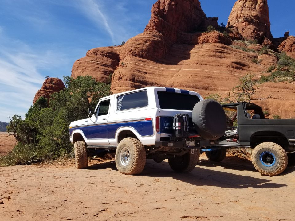 White and blue Ford Bronco parked on a dirt trail with red rock formations in the background.