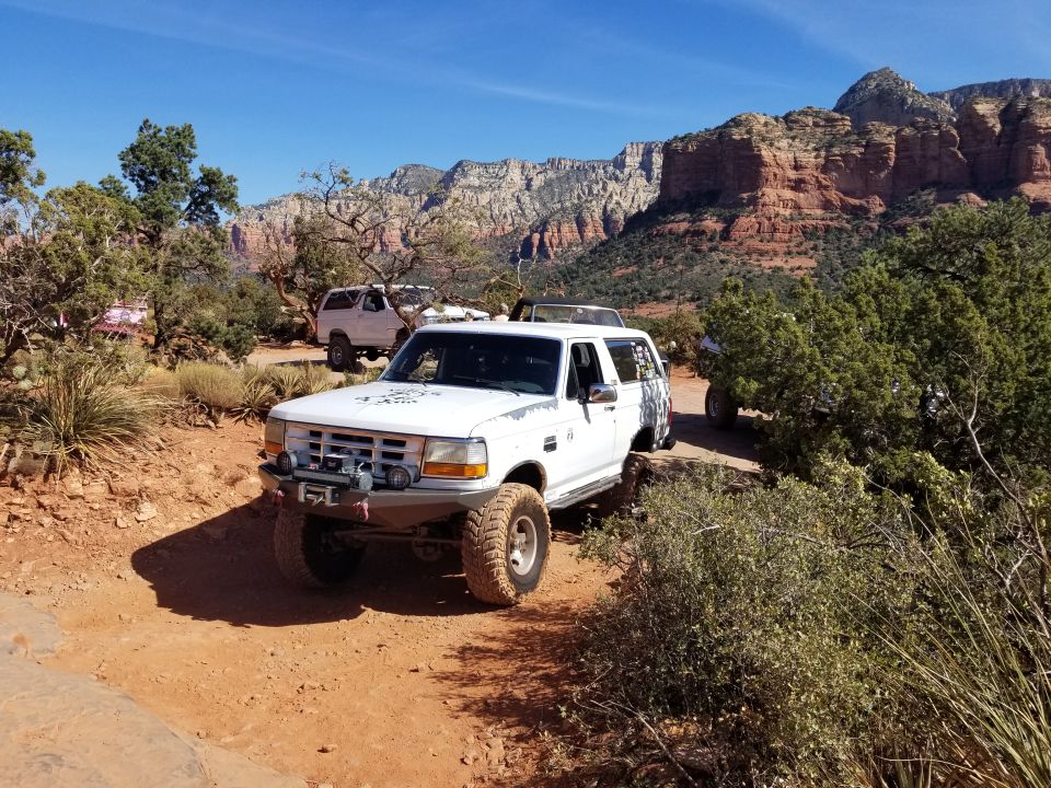 White 1995 Ford Bronco with off-road tires and winch parked on a dirt trail in Sedona, Arizona.