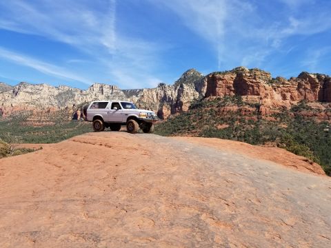 1995 Ford Bronco - A white 1995 Ford Bronco is parked on a large, reddish-orange rock formation with a scenic backdrop of red rock cliffs and a blue sky with…