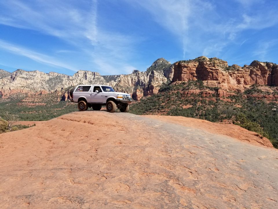 White 1995 Ford Bronco parked on a red rock formation with Sedona cliffs in the background.