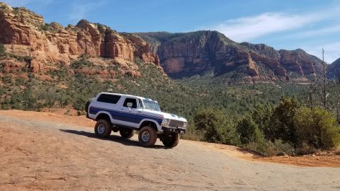1995 Ford Bronco - A lifted, classic white and blue Ford Bronco is parked on a rocky, red dirt trail with a scenic canyon and mountainous backdrop under a cle…