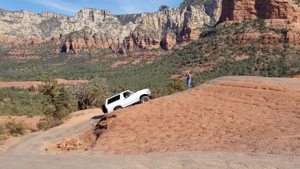 White 1995 Ford Bronco climbing a steep dirt trail with a person watching.