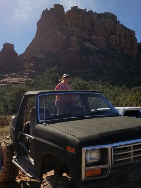 1995 Ford Bronco - A woman wearing a colorful shirt and a baseball cap stands in the open doorway of a black, lifted Ford Bronco. The vehicle is parked in a r…