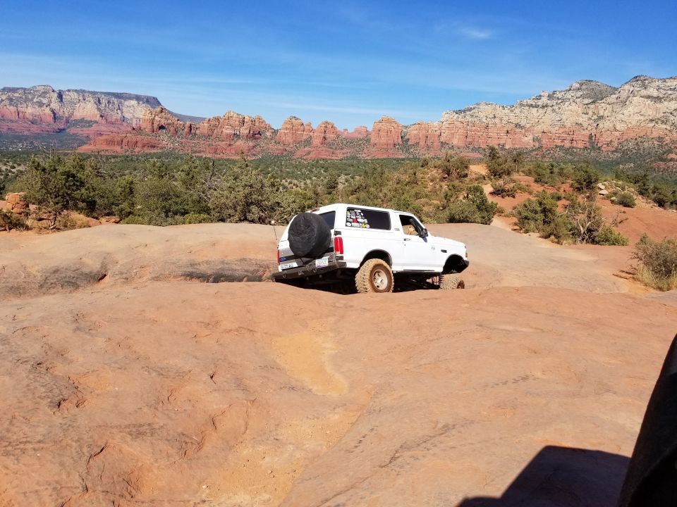 White 1990s Ford Bronco on a rocky trail with red rock mountains.