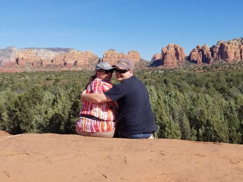 1995 Ford Bronco - A couple embraces while sitting on a rock formation with a scenic view of red rock formations and green trees under a clear blue sky.