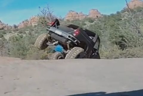1995 Ford Bronco - A heavily modified black off-road truck is tilted precariously on a dirt hill, with its front tires high in the air. The vehicle is navigat…