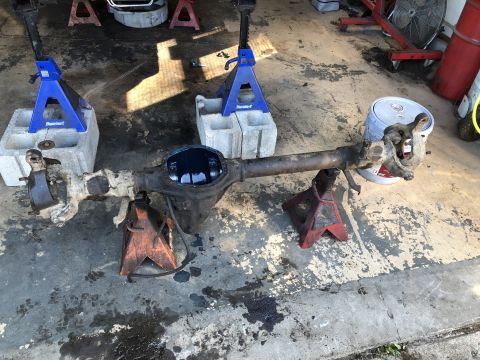 1995 Ford F-150 - A disassembled rear axle assembly is supported by jack stands on a concrete floor. The differential cover is removed, revealing dark fluid…