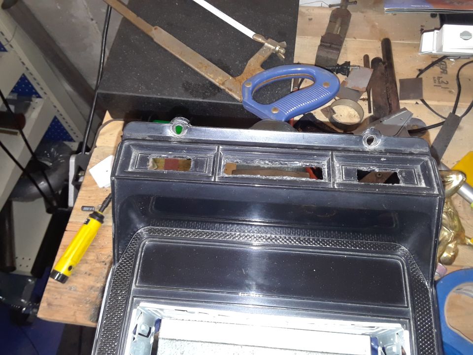 Black and chrome vehicle dashboard trim with three cutouts and a yellow soldering iron.