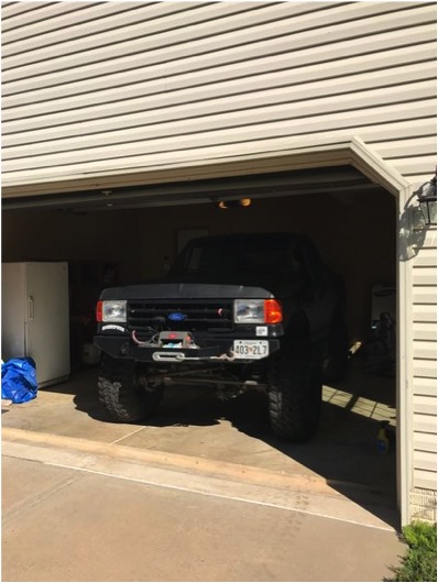 1989 Ford Bronco - A lifted, dark-colored Ford Bronco is parked inside an open garage. The front of the vehicle is visible, featuring a winch mounted on the b…