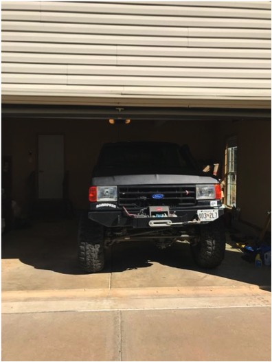 1989 Ford Bronco - A lifted, dark-colored Ford Bronco is parked inside a garage with the door open. The front of the vehicle features a winch mounted on a cus…