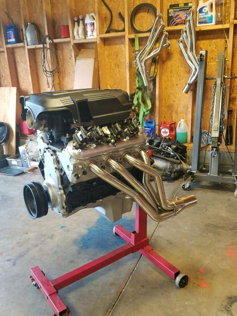 V8 engine with chrome headers on a red engine stand in a garage.
