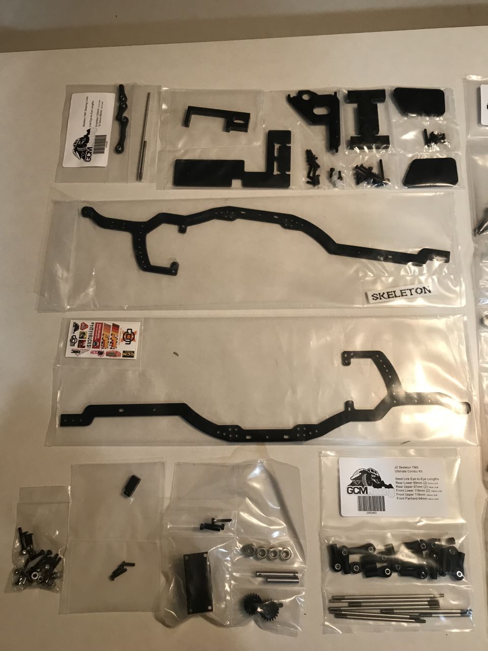 RC car chassis parts including black metal rails, screws, gears, and labels.