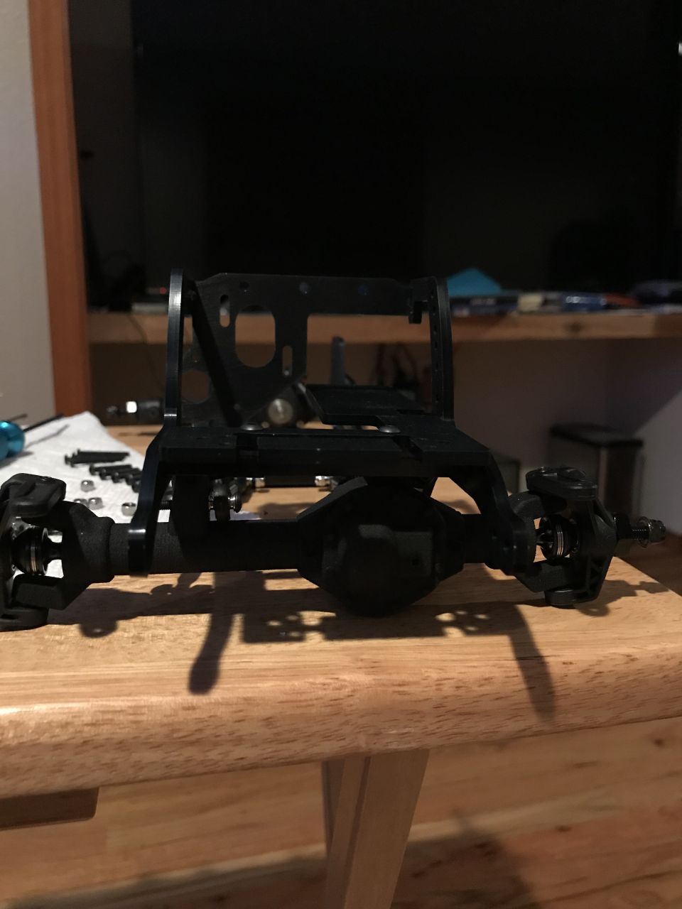 Black vehicle chassis and axle assembly on a wooden table.
