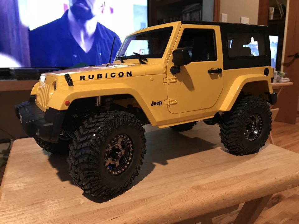 Yellow RC Jeep Wrangler Rubicon with black top and large tires on a wooden table.