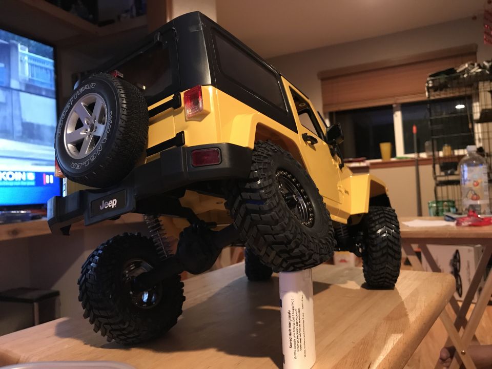 Yellow RC Jeep Wrangler with black roof, spare tire, and elevated rear wheel.