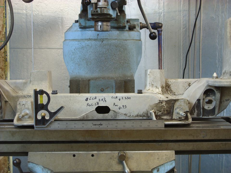 Metal component with measurements on a workbench next to a ruler and machinist's square.