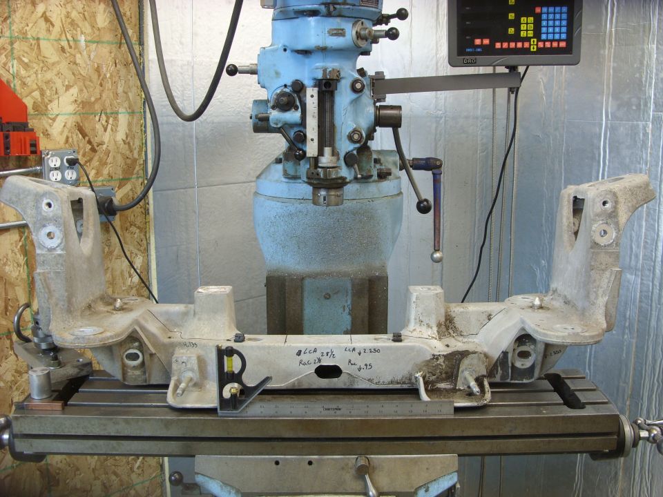 Aluminum front subframe assembly on a milling machine table, with measurement markings