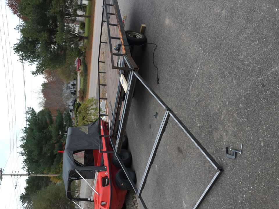 Red amphibious vehicle with black canopy on a trailer, parked on asphalt