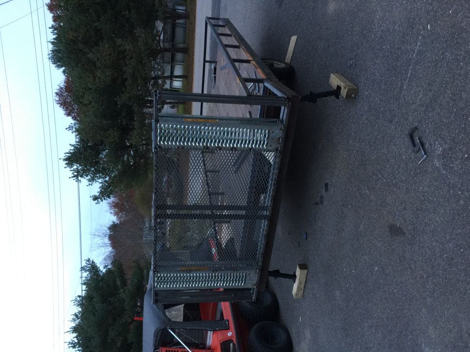 Trailer with metal cage and ramp, parked on asphalt