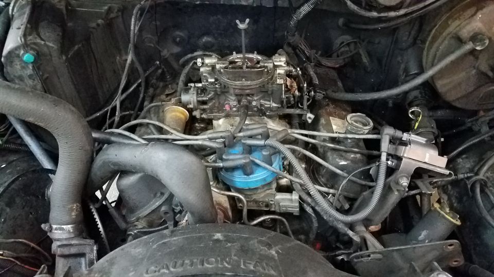 Engine bay with carburetor, distributor, and hoses visible. Fan shroud has text