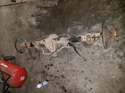 1996 Ford Bronco - A disassembled rear axle assembly rests on a garage floor next to an air compressor.