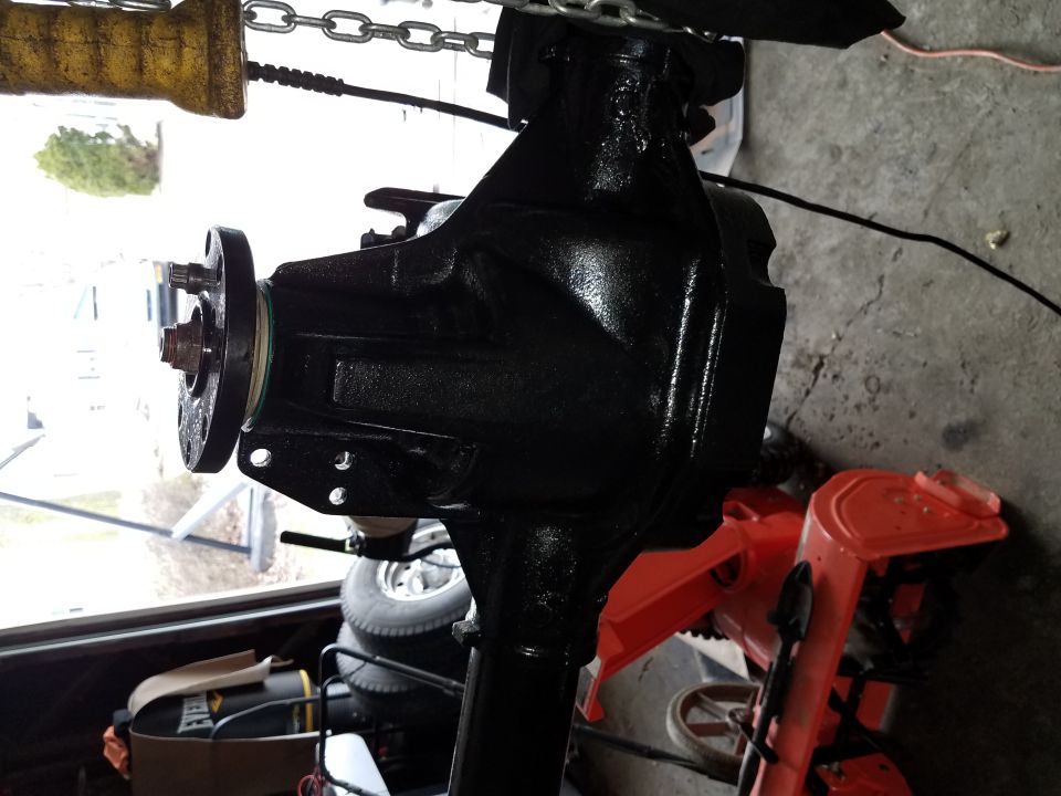 Black differential housing with flange and bolt assembly, garage setting with chain hoist.