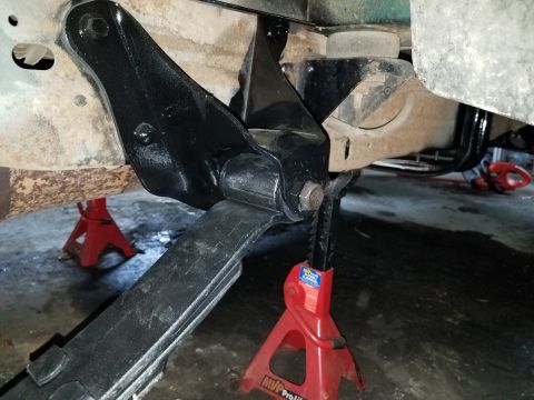 1996 Ford Bronco - A close-up view of the undercarriage of a vehicle, focusing on a black leaf spring suspension component being supported by a red jack stand…