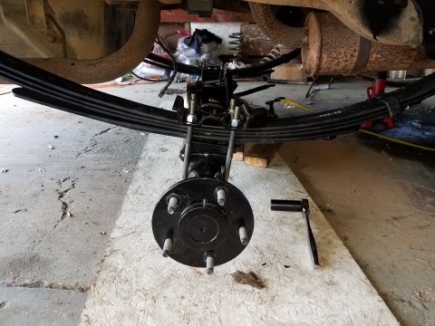 1996 Ford Bronco - A close-up view of a vehicle's rear suspension assembly, including leaf springs, U-bolts, and a hub, with a socket wrench resting on a wood…