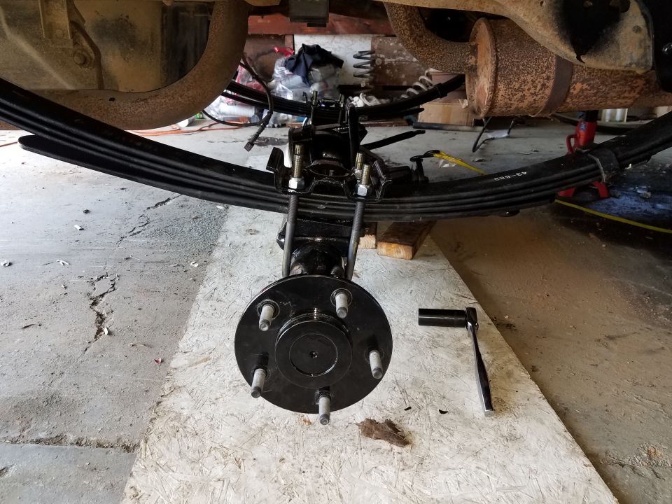 Vehicle rear suspension with leaf springs, hub, and socket wrench.
