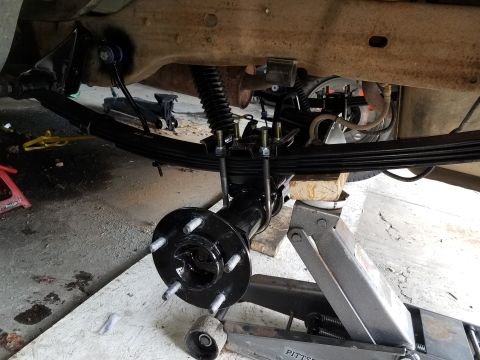 1996 Ford Bronco - The underside of a vehicle is shown with the rear axle assembly being supported by a floor jack and wooden blocks. A leaf spring suspension…