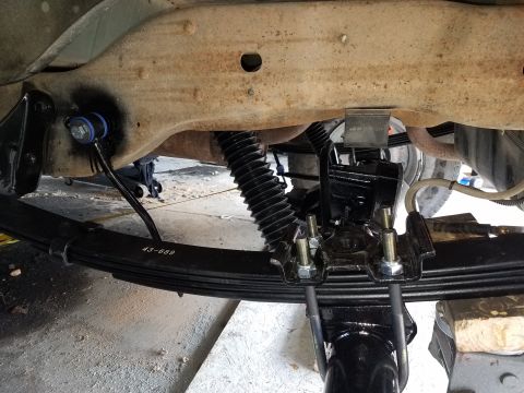 1996 Ford Bronco - A close-up view of the rear suspension of a vehicle, showing a new leaf spring assembly with U-bolts and hardware attached to the axle. The…