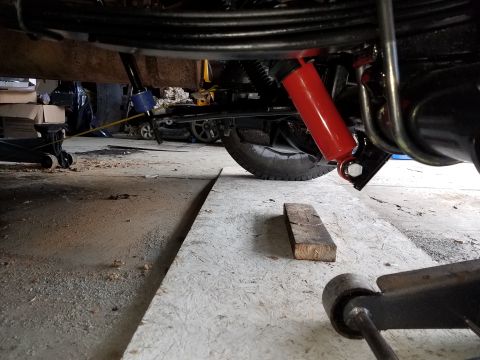 1996 Ford Bronco - Underneath view of a vehicle's rear suspension, showing a red shock absorber mounted to the axle and frame. A hydraulic jack is visible in…
