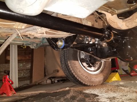 1996 Ford Bronco - The underside of a vehicle shows a black driveshaft connected to a differential, with a blue and yellow bushing visible on a suspension com…