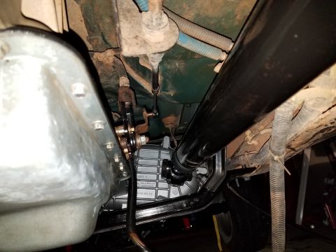 1996 Ford Bronco - Underside view of a vehicle's transmission and driveshaft. A silver transmission pan is visible on the left, with a black driveshaft extend…