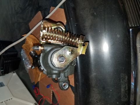 1996 Ford Bronco - A close-up view of a brake caliper assembly with a large yellow spring attached, resting on cardboard.
