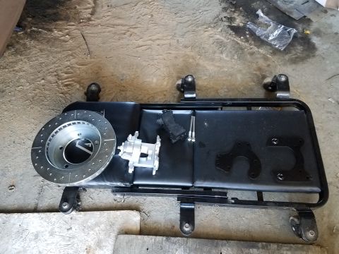 1996 Ford Bronco - A drilled and slotted brake rotor and a brake caliper are laid out on a black creeper seat. Several black metal mounting brackets and bolts…