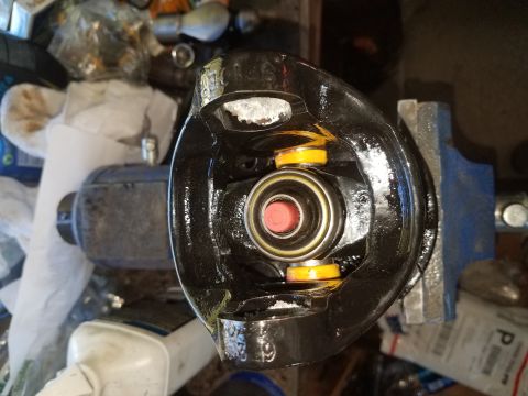 1996 Ford Bronco - A close-up view of a U-joint assembly, likely for a 1996 Ford Bronco, held in a vise. The U-joint is black and appears to have yellow and r…