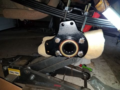 1996 Ford Bronco - A close-up view of a black suspension part with a bearing, attached to U-bolts above a hydraulic jack. The part appears to be a hub assembl…
