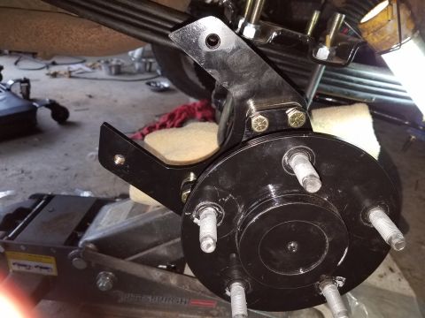 1996 Ford Bronco - A black brake caliper mounting bracket is bolted to a black hub assembly with multiple studs, attached to a leaf spring suspension system.…