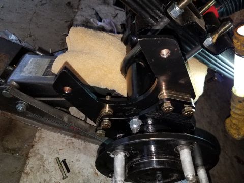 1996 Ford Bronco - A black metal bracket is bolted to a vehicle's suspension and hub assembly, which is supported by a hydraulic floor jack. The bracket has s…