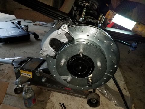 1996 Ford Bronco - A close-up view of a newly installed rear brake rotor and caliper assembly on a vehicle, supported by a hydraulic floor jack. The brake rot…