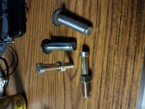 1996 Ford Bronco - Four metal fasteners are laid out on a wooden surface. Three of the fasteners are cylindrical pins with flared heads, and one is a bolt wit…