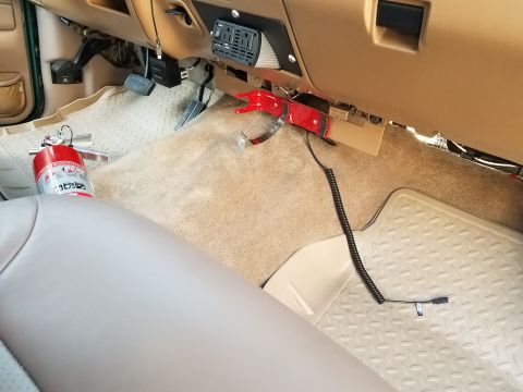 1996 Ford Bronco - The interior of a vehicle shows a red fire extinguisher mounted on the floor next to the driver's seat. A black coiled cord with a connecto…