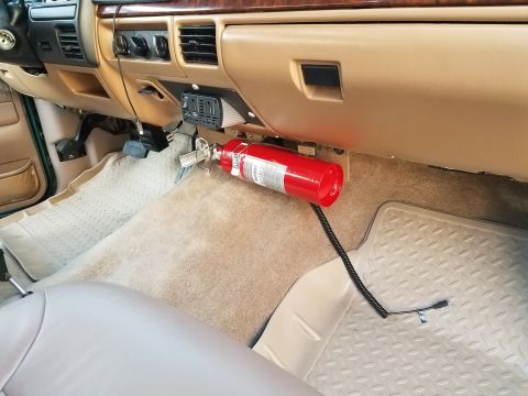 1996 Ford Bronco - The interior of a vehicle shows a red fire extinguisher mounted below the dashboard, to the right of the steering column. A black coiled co…