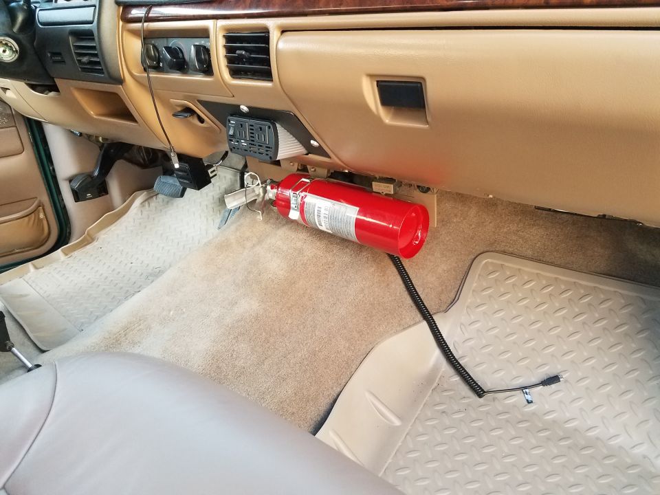Interior view of a vehicle showing a fire extinguisher and power inverter mounted on the dashboard.