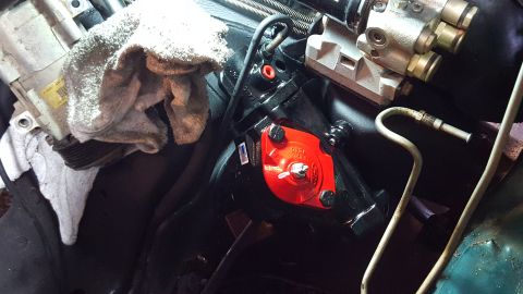 1996 Ford Bronco - A close-up view of a red power steering gearbox with black bolts is visible, mounted on a black component. A rag is draped over a silver co…