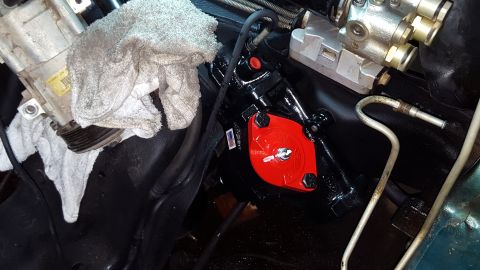 1996 Ford Bronco - A close-up view of a newly installed black steering gear box with a bright red cap, bolted to the vehicle's frame. A white rag is draped ov…