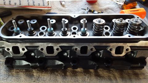 1996 Ford Bronco - A close-up view of a black V8 engine cylinder head with valves and valve springs installed. The engine head is resting on a gray textured s…